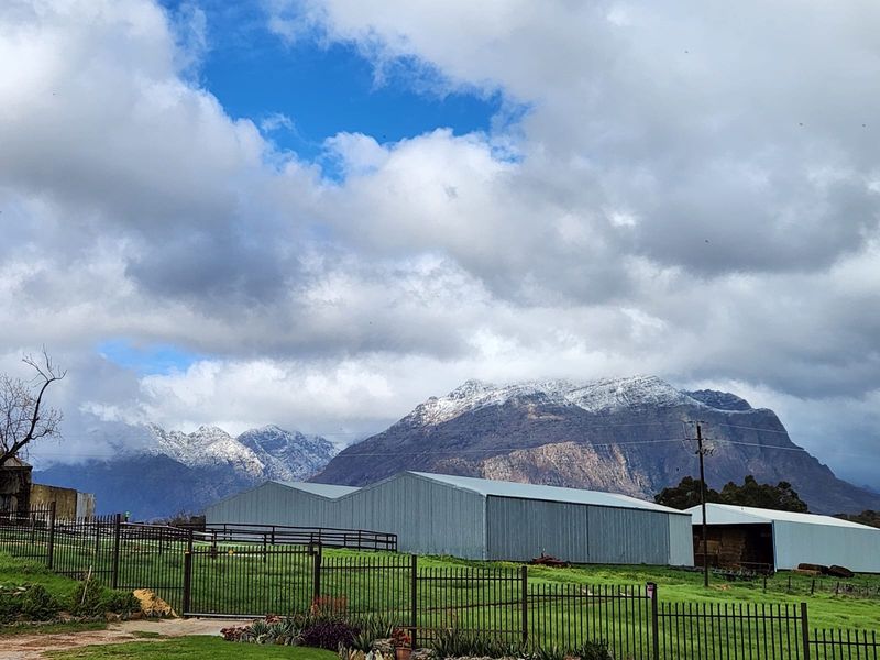 Scenic view of the farm property featuring large metal agricultural sheds set against a backdrop of snow-capped mountains.