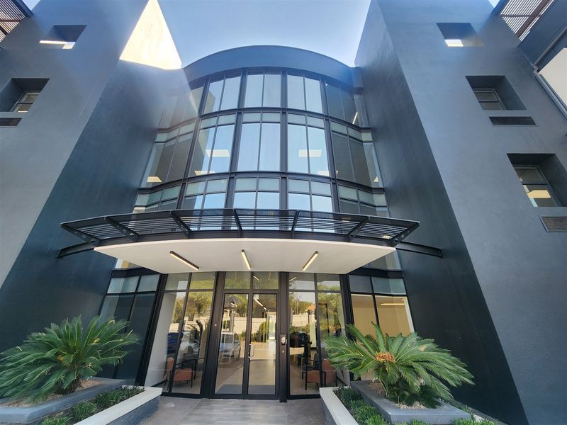 Modern office building entrance featuring a striking glass facade, sleek metal canopy, and professional landscaping.