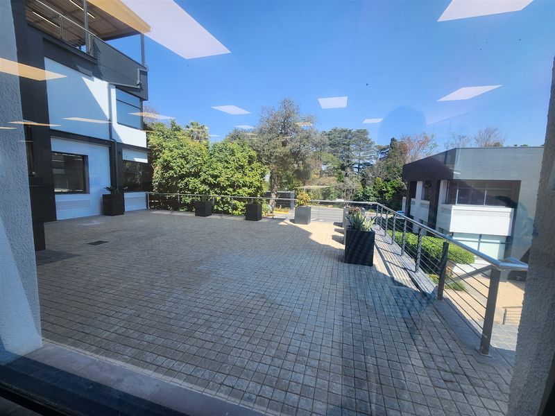 A spacious outdoor terrace featuring paved flooring and stainless steel railings, offering a view of the surrounding office building exterior and landscaped grounds.