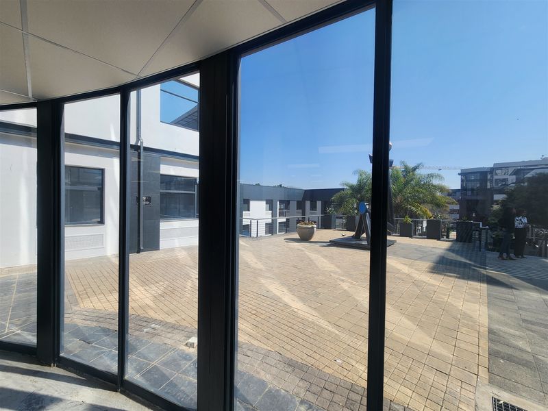 A view from an interior office space looking out onto a paved outdoor terrace area with modern architectural finishes.
