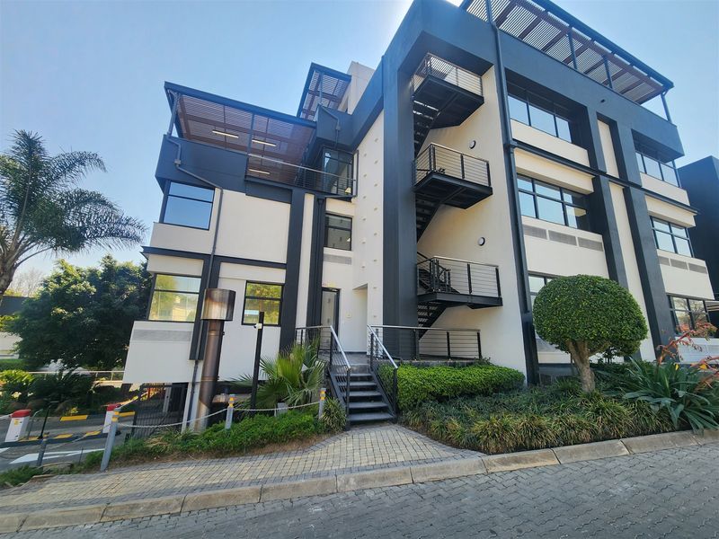 Modern multi-story office building featuring a contemporary facade, external steel staircase, balconies with pergolas, and well-maintained landscaped surroundings.