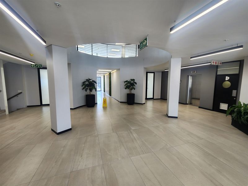 Modern office building lobby featuring tiled flooring, recessed linear lighting, a central circular ceiling feature, and elevator access.