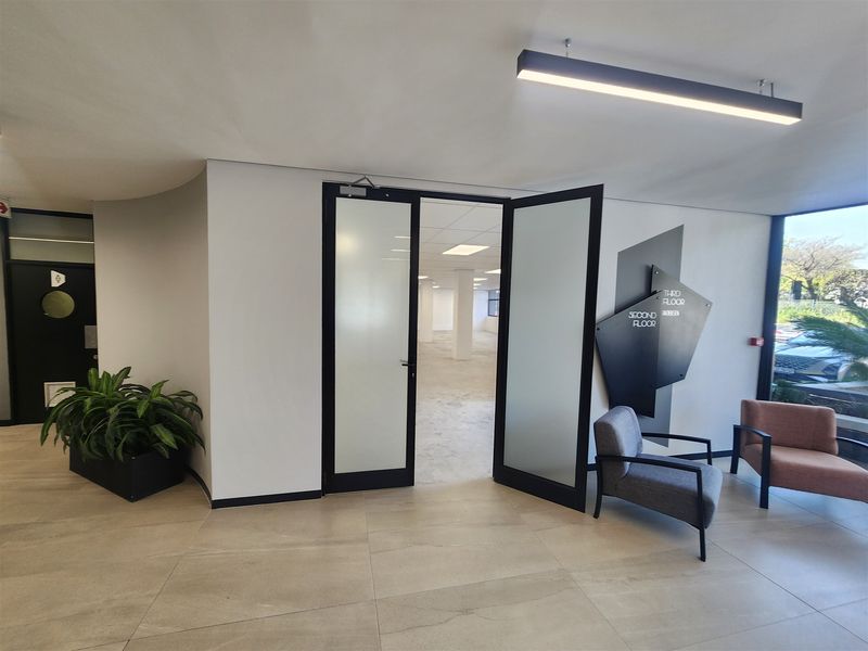 Modern office building entrance lobby featuring tiled flooring, contemporary linear lighting, and clear directional signage leading to the main office floor.