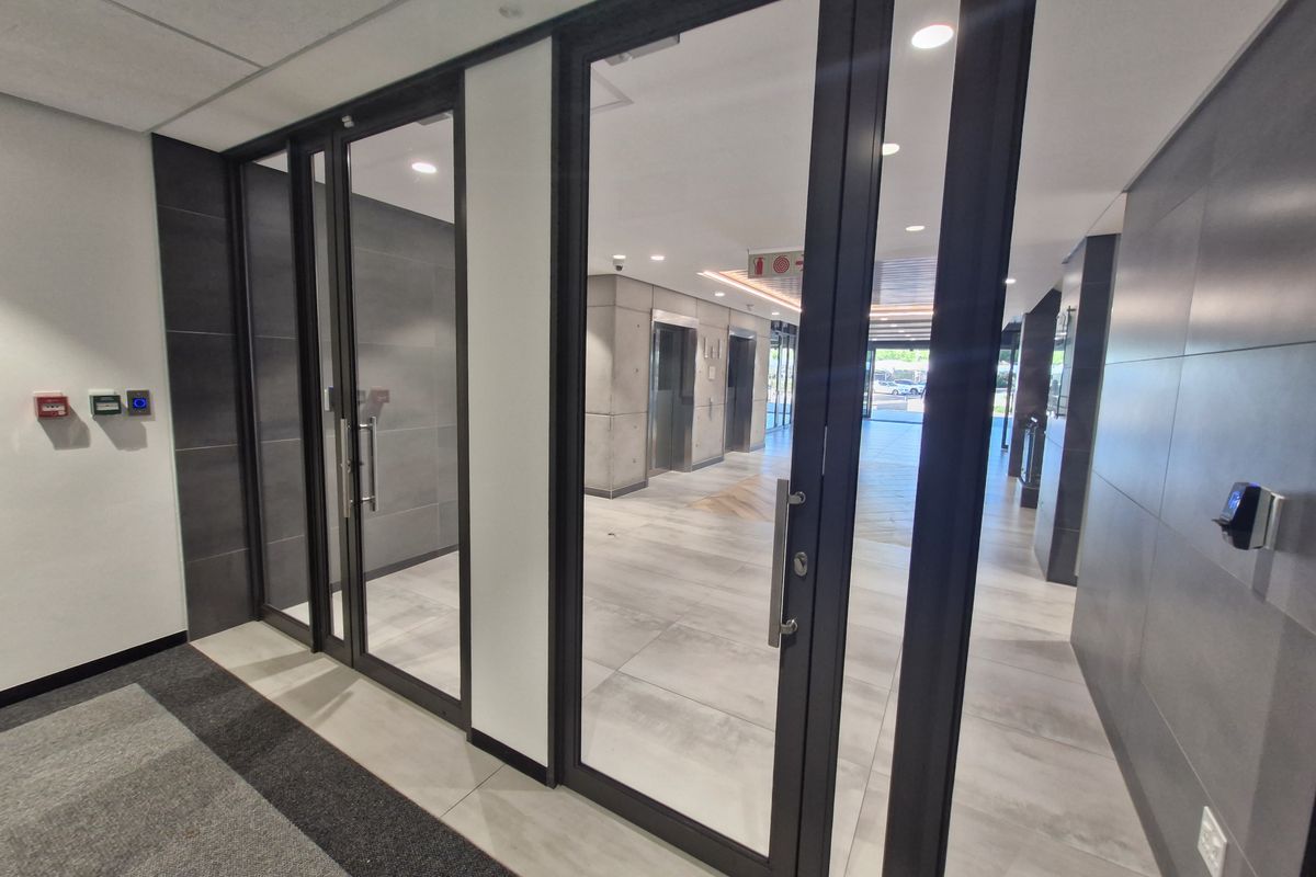 Modern commercial building entrance lobby featuring glass-panelled doors, tiled flooring, and professional elevator access area with contemporary finishes.