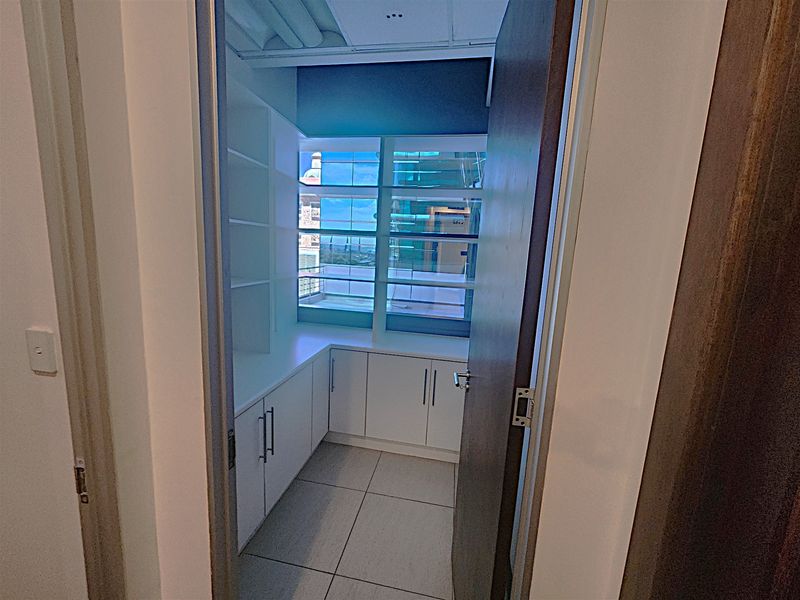 A compact, well-lit office space featuring built-in white cabinetry, shelving, and large windows providing natural light and exterior views.