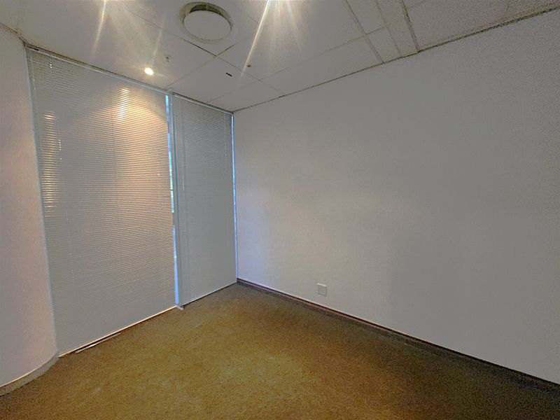 An empty office space featuring a suspended ceiling, recessed lighting, venetian blinds, and carpeted flooring.