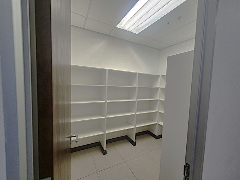 A clean, functional utility or storage room featuring built-in white shelving, tiled flooring, and overhead fluorescent lighting.
