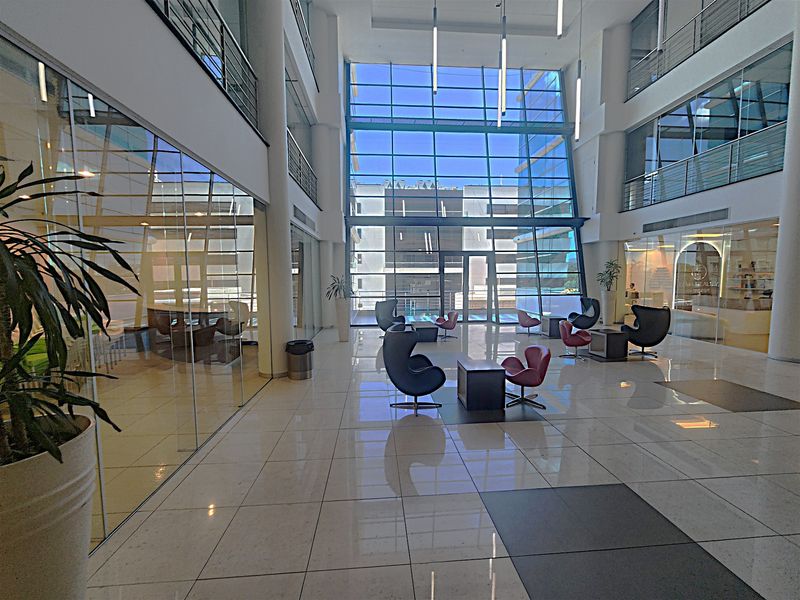 Spacious modern office building atrium featuring high ceilings, extensive glass curtain walling, polished tile floors, and a bright, open-plan reception area.