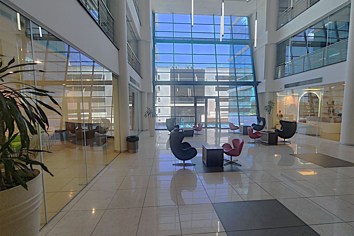Spacious modern office building atrium featuring high ceilings, extensive glass curtain walling, polished tile floors, and a bright, open-plan reception area.