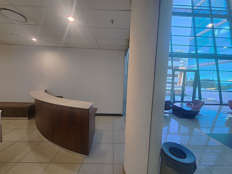 Modern office entrance featuring a curved built-in reception desk, tiled flooring, and expansive floor-to-ceiling glass windows providing natural light.