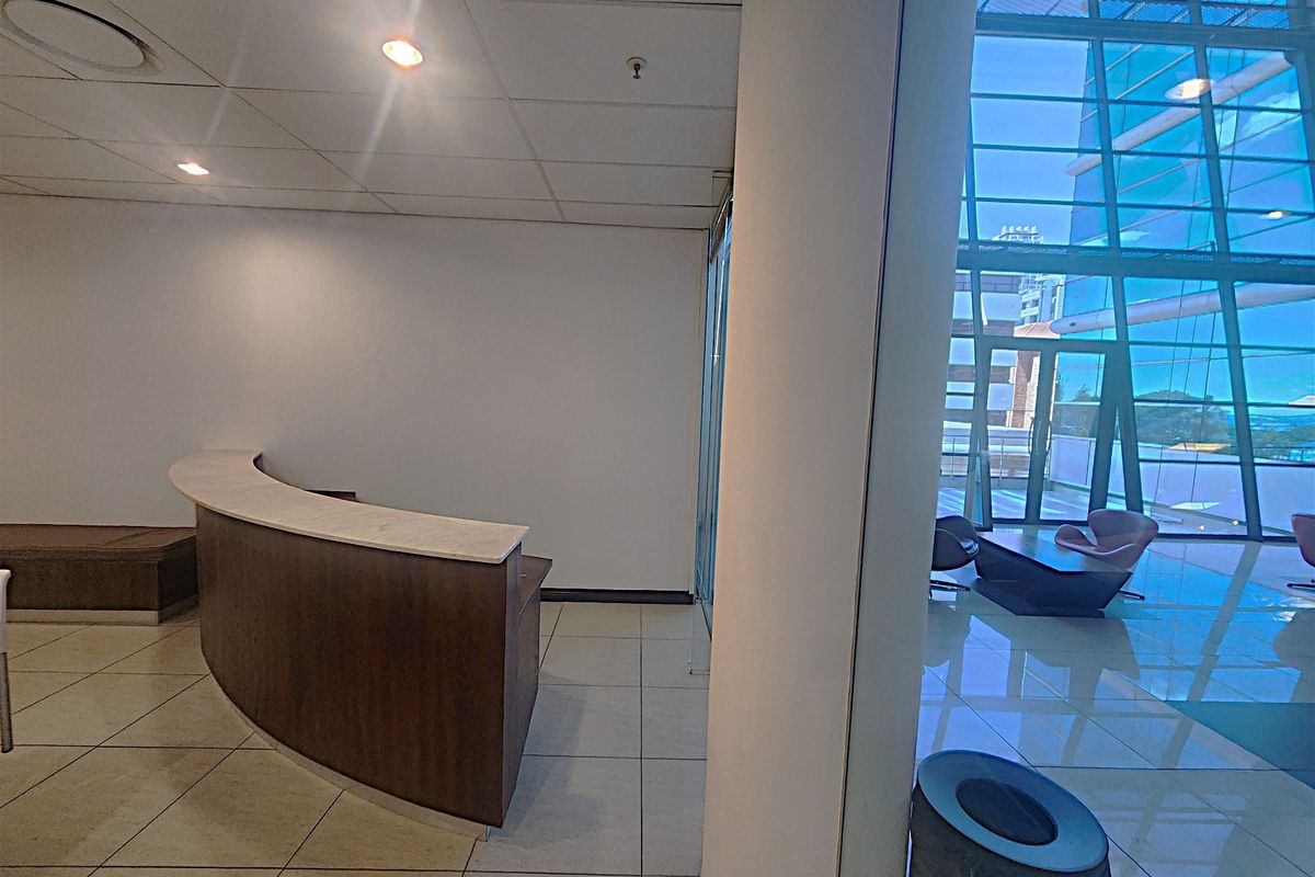 Modern office entrance featuring a curved built-in reception desk, tiled flooring, and expansive floor-to-ceiling glass windows providing natural light.