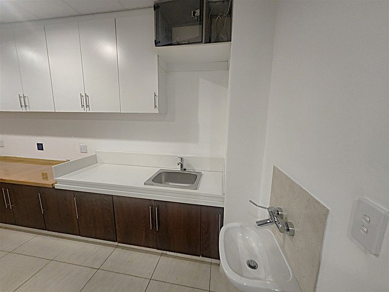 A functional office kitchenette featuring built-in cabinetry, a stainless steel sink, and a separate wall-mounted basin with tiled flooring.