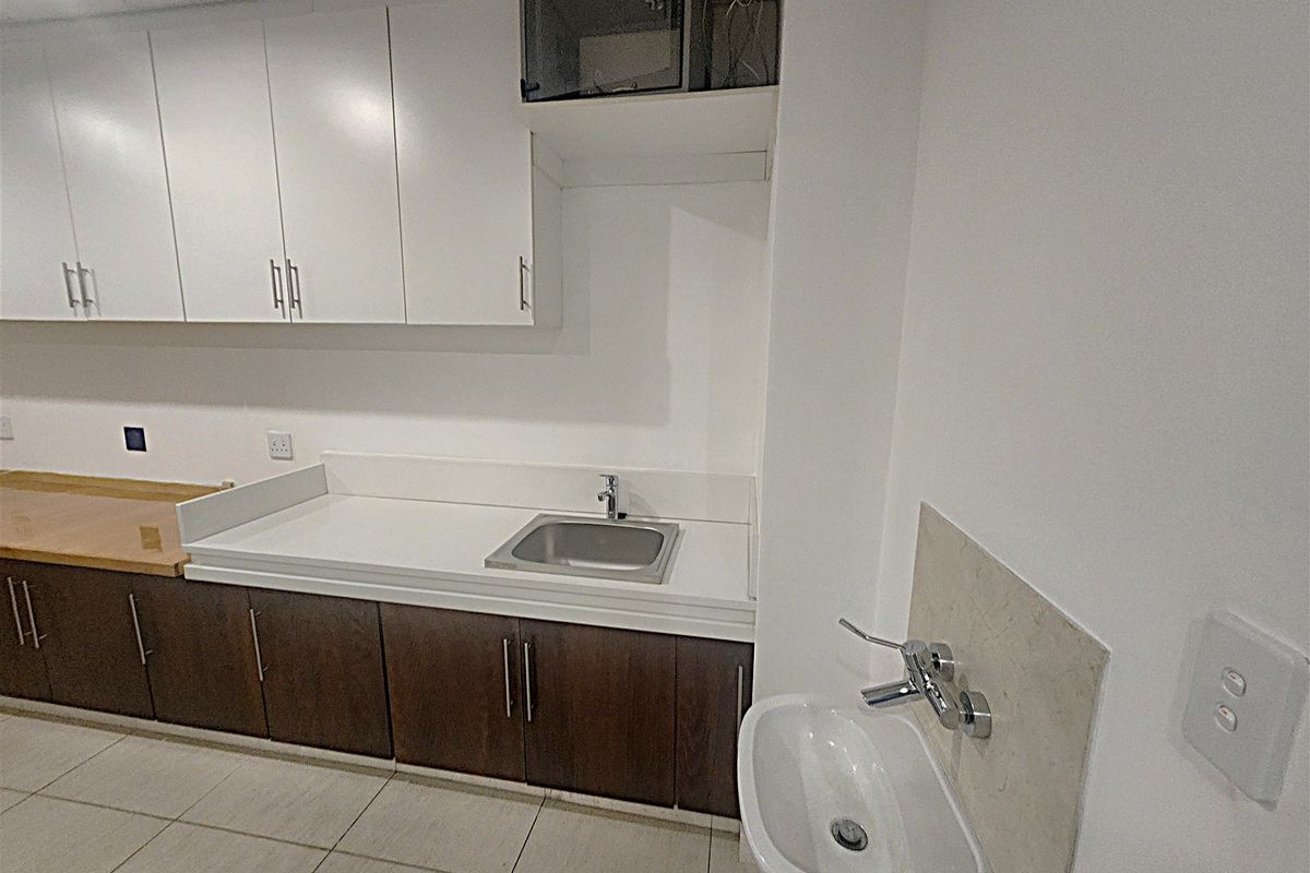A functional office kitchenette featuring built-in cabinetry, a stainless steel sink, and a separate wall-mounted basin with tiled flooring.