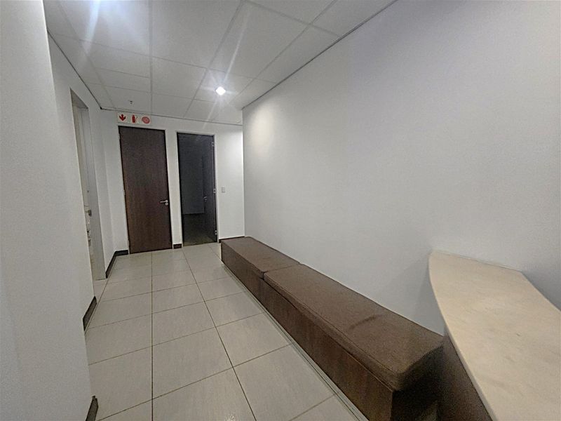 A clean office hallway featuring tiled flooring, a suspended ceiling with recessed lighting, and built-in bench seating along the wall.