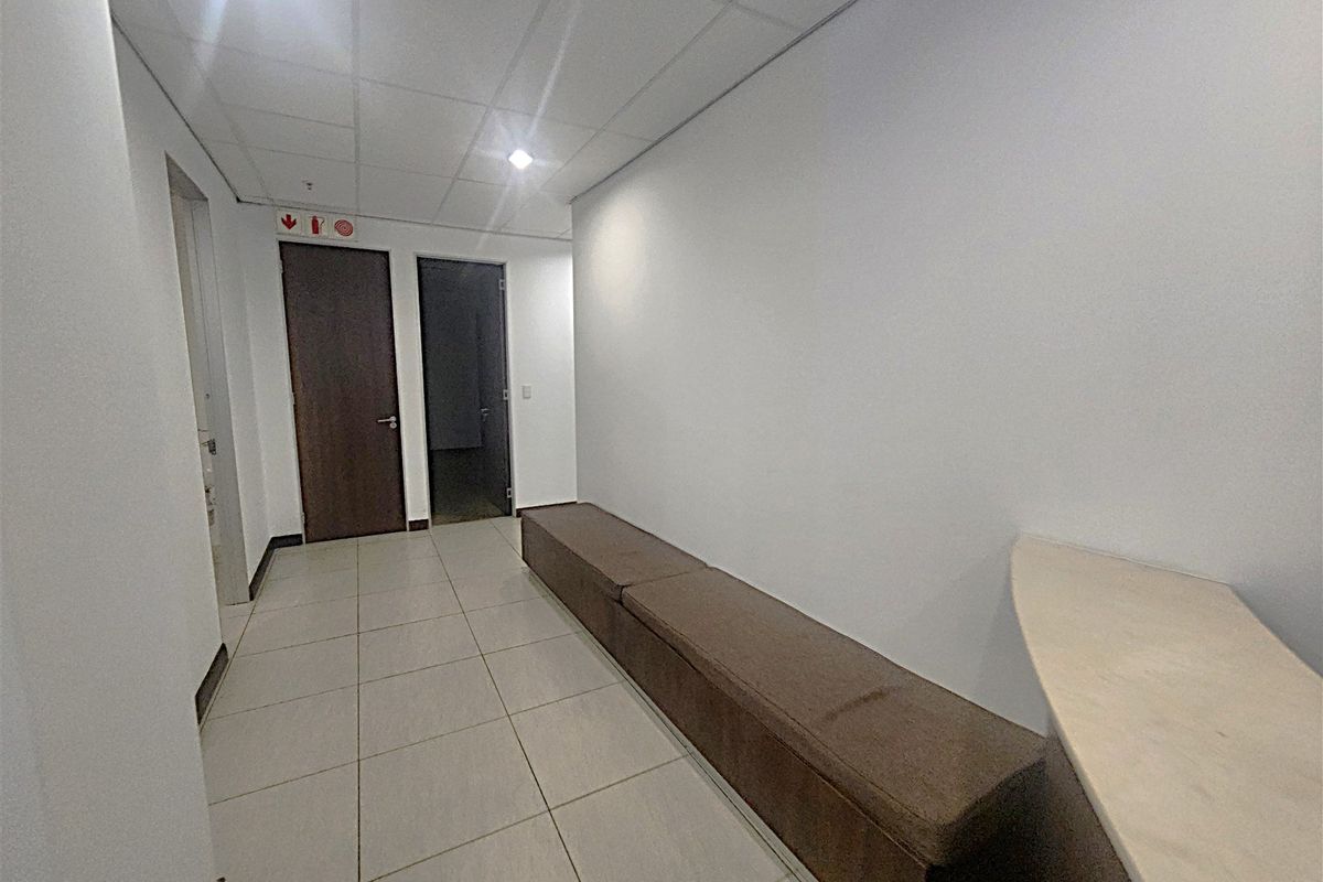 A clean office hallway featuring tiled flooring, a suspended ceiling with recessed lighting, and built-in bench seating along the wall.