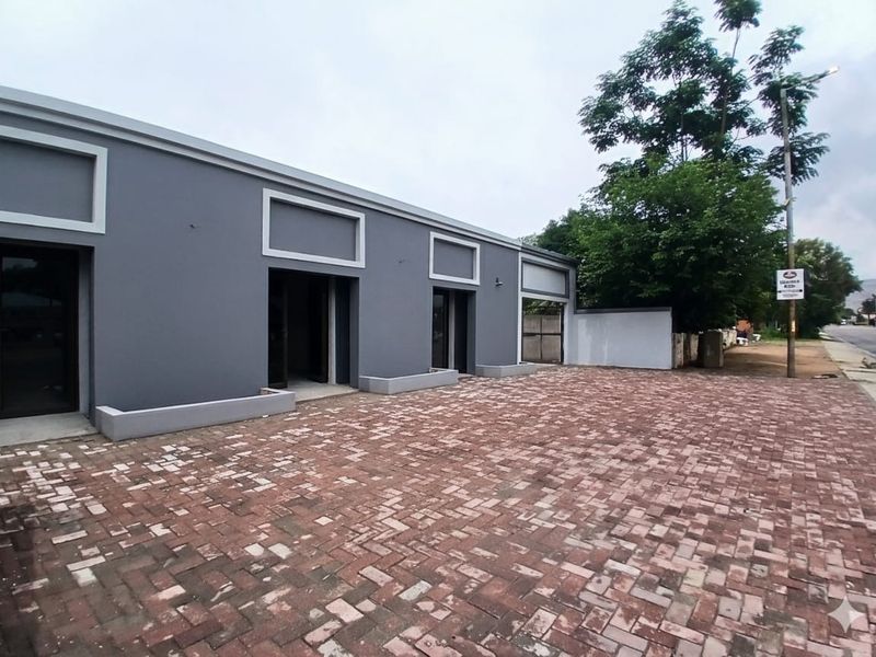Front exterior view of a modern office building featuring a paved driveway, built-in planters, and multiple entrance points.