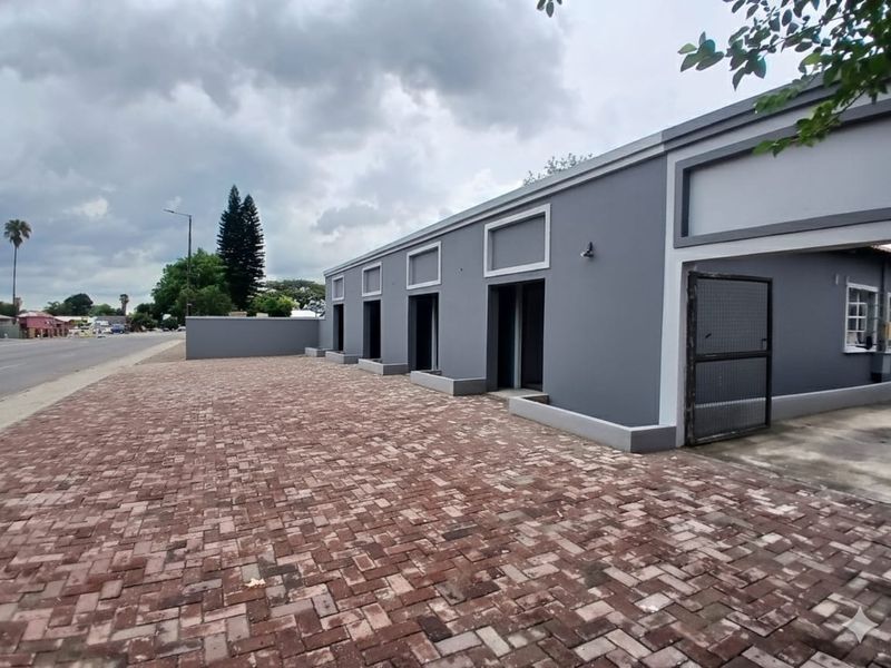 A modern office exterior featuring a freshly painted grey facade, paved driveway, and secure gated access, situated along a street-front property.