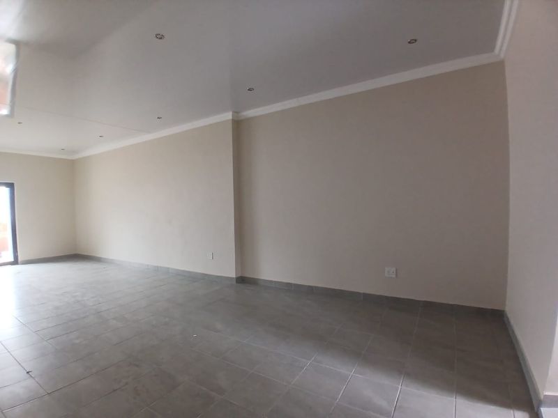 A spacious, empty office area featuring neutral walls, tiled flooring, and recessed ceiling lighting, providing a clean and versatile workspace.