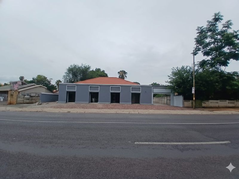 Front exterior view of a commercial office building featuring a grey facade, terracotta tiled roof, and paved frontage along a main road.