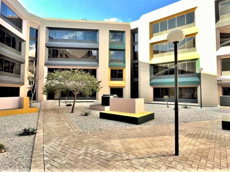 A well-maintained office courtyard featuring paved walkways, gravel landscaping, built-in concrete seating, and a modern multi-story building facade with tinted windows.
