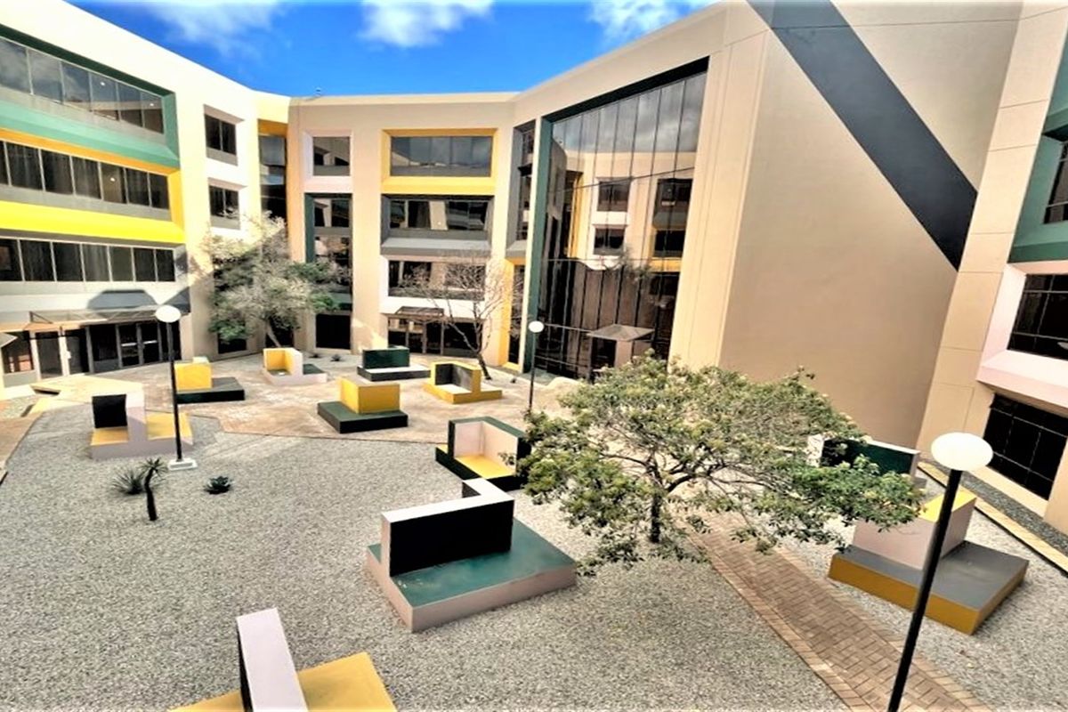 A modern office building courtyard featuring a central landscaped area with paved paths, gravel surfacing, and large glass facade elements.
