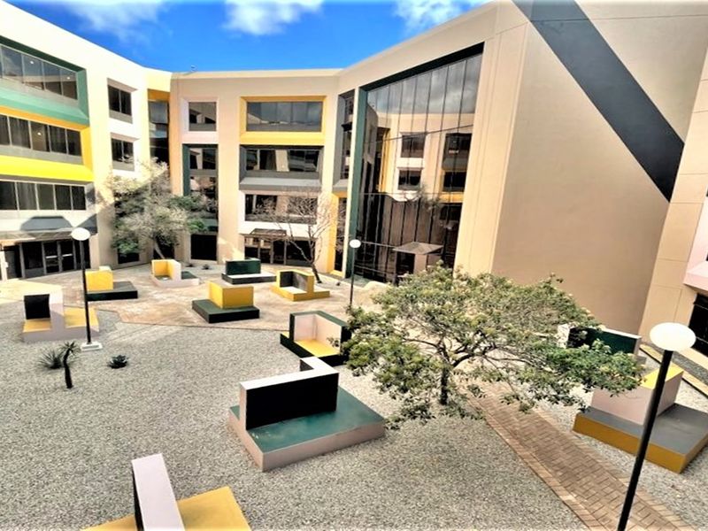 A modern office building courtyard featuring a central landscaped area with paved paths, gravel surfacing, and large glass facade elements.