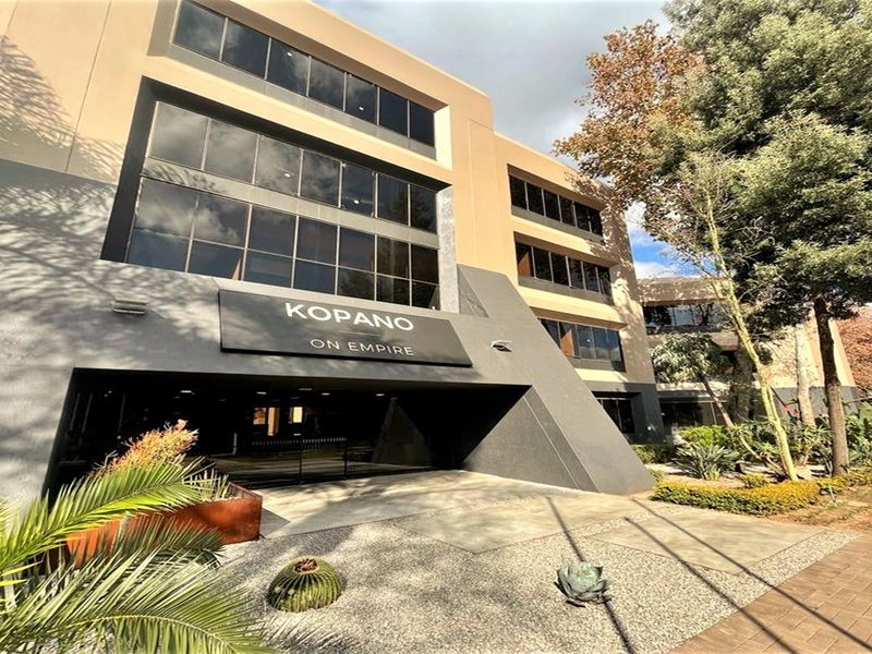 Modern multi-story office building facade featuring tinted glass windows, professional signage, and a well-maintained landscaped entrance area.