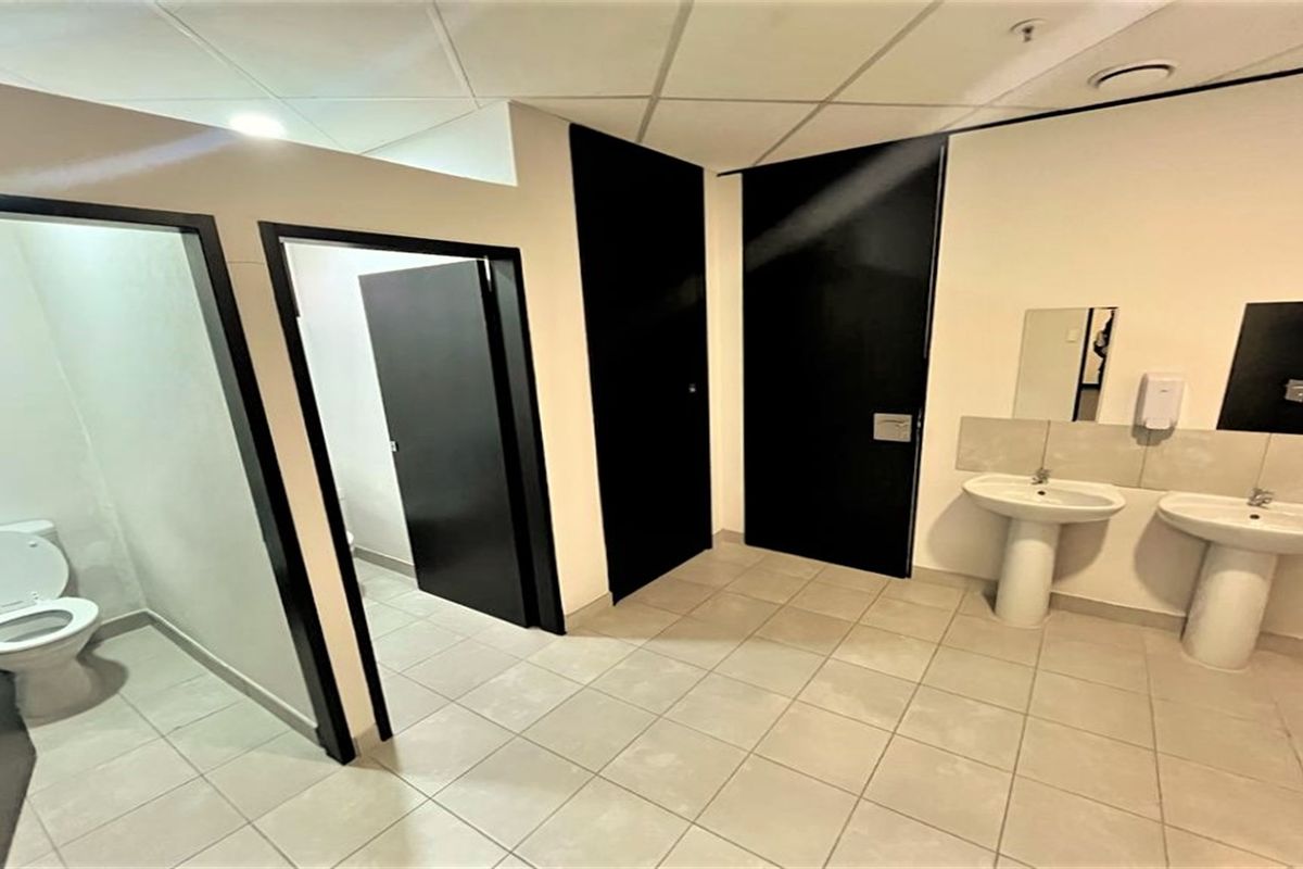 A clean, functional commercial bathroom facility featuring dual pedestal wash basins, tiled flooring, and separate toilet cubicles with modern black doors.