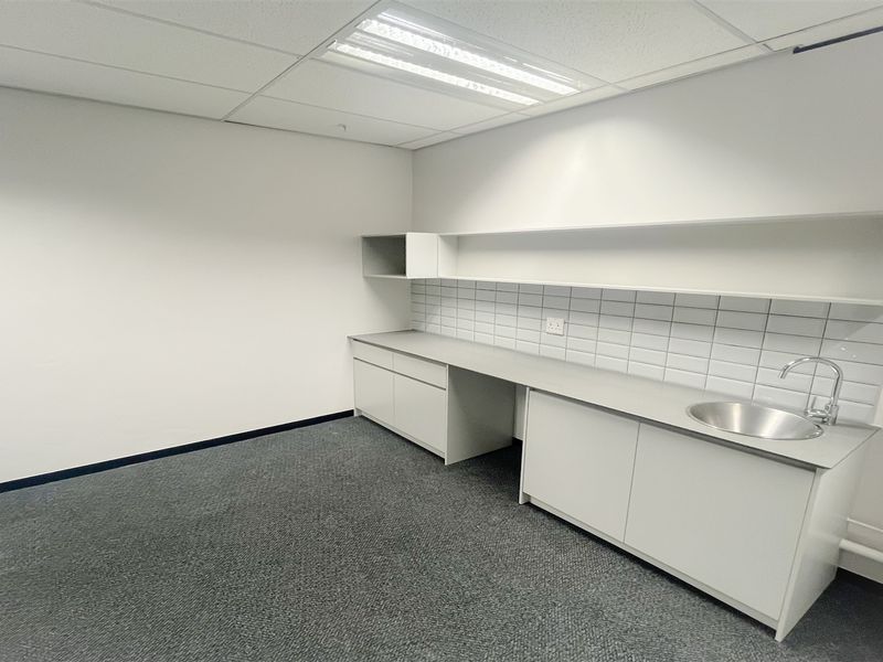 A clean, empty utility or kitchenette space featuring built-in cabinetry, a stainless steel sink, tiled backsplash, and functional overhead lighting.