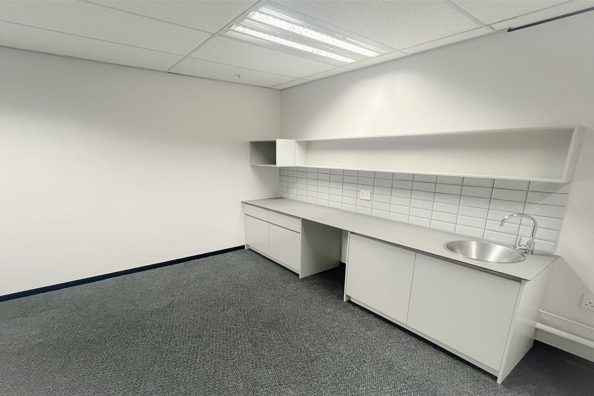 A clean, empty utility or kitchenette space featuring built-in cabinetry, a stainless steel sink, tiled backsplash, and functional overhead lighting.