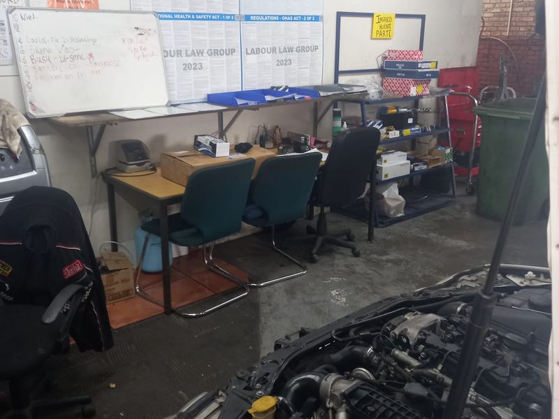 A functional workshop or utility area featuring exposed brickwork, concrete flooring, and integrated wall-mounted shelving for industrial or automotive maintenance tasks.