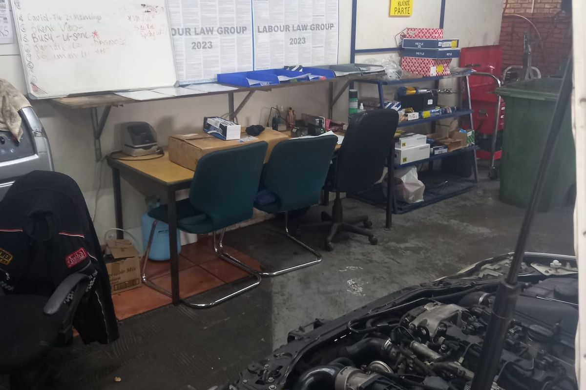 A functional workshop or utility area featuring exposed brickwork, concrete flooring, and integrated wall-mounted shelving for industrial or automotive maintenance tasks.
