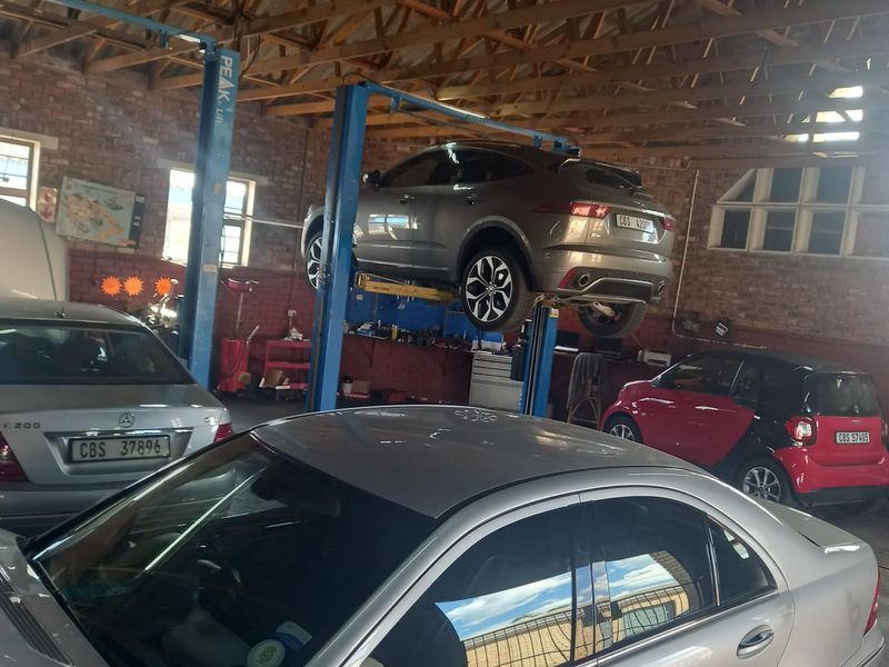 A functional automotive workshop featuring exposed brick walls, timber roof trusses, and a professional two-post vehicle lift for maintenance and repair services.