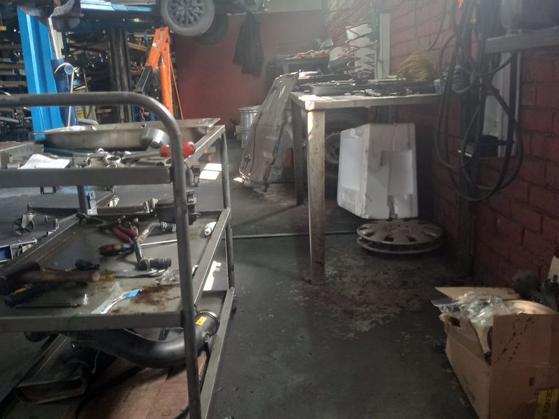 A functional automotive workshop space featuring exposed brick walls, concrete flooring, and an integrated vehicle lift system.