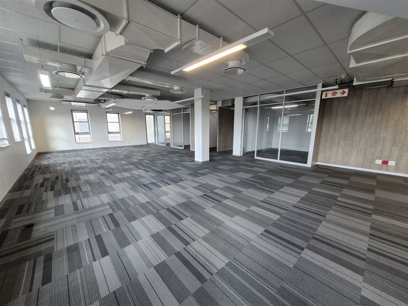 Spacious open-plan office area featuring modern carpet tiles, suspended ceilings with exposed ducting, and glass-partitioned meeting rooms.