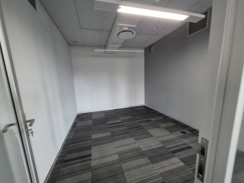 A clean, empty office space featuring a suspended ceiling, integrated lighting, air conditioning vents, and modern grey carpet tiles.
