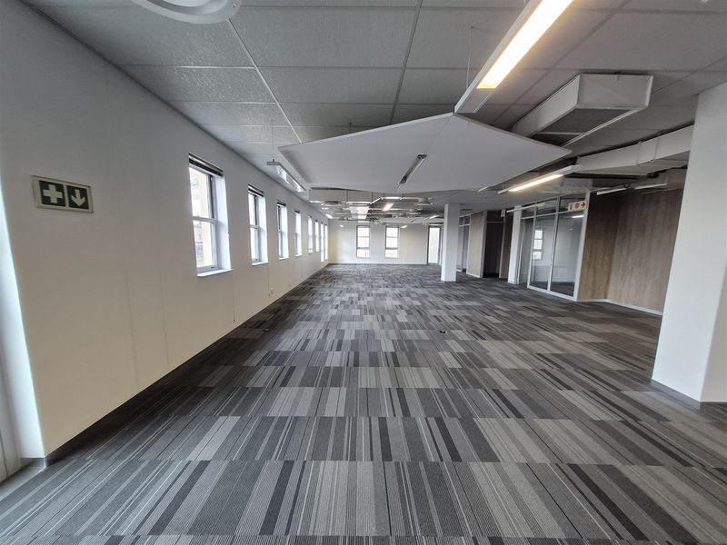 A spacious, open-plan office area featuring modern carpet tiles, suspended ceilings with integrated lighting, and glass-partitioned meeting rooms.