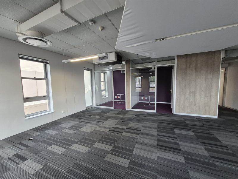 Modern open-plan office space featuring glass partitions, carpeted flooring, suspended ceilings, and integrated air conditioning, offering a professional and versatile work environment.