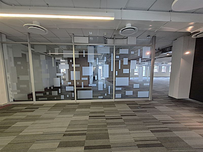 Spacious open-plan office area featuring modern glass partitioning, suspended ceilings with integrated lighting, and durable carpet tile flooring.