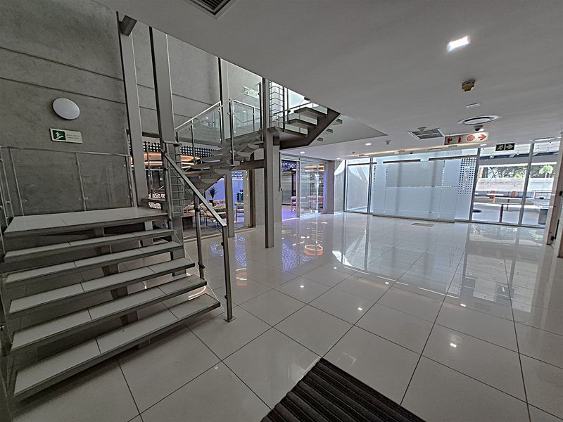 Modern office building entrance lobby featuring a striking open-tread staircase with glass balustrades, polished tile flooring, and expansive glass partitions.