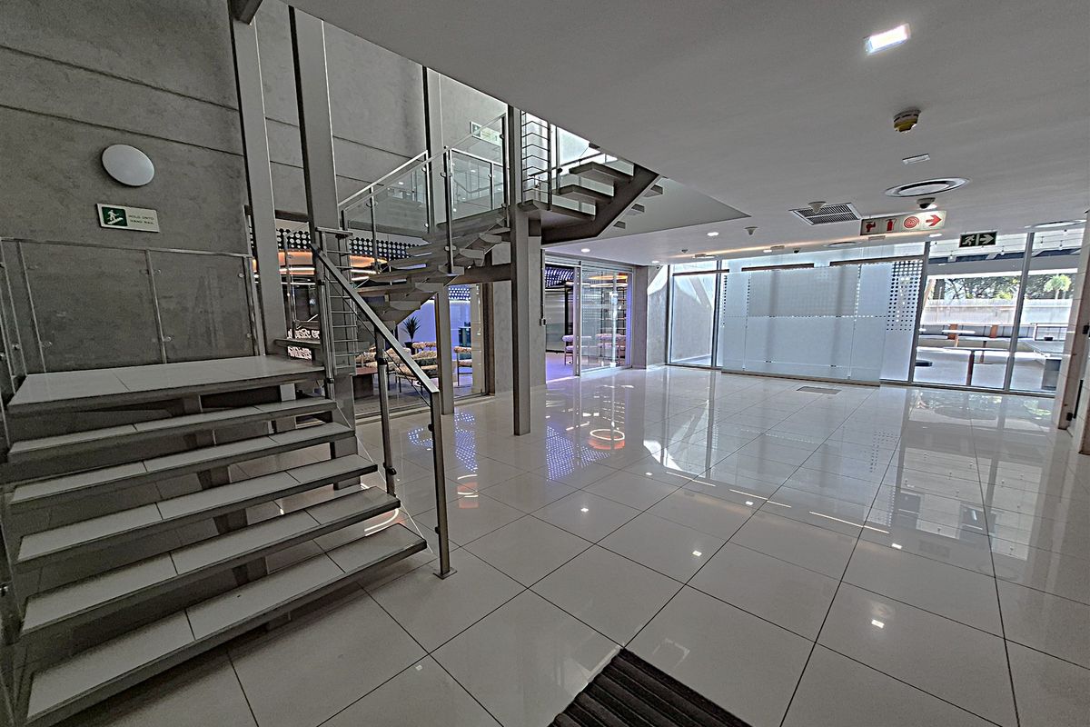 Modern office building entrance lobby featuring a striking open-tread staircase with glass balustrades, polished tile flooring, and expansive glass partitions.