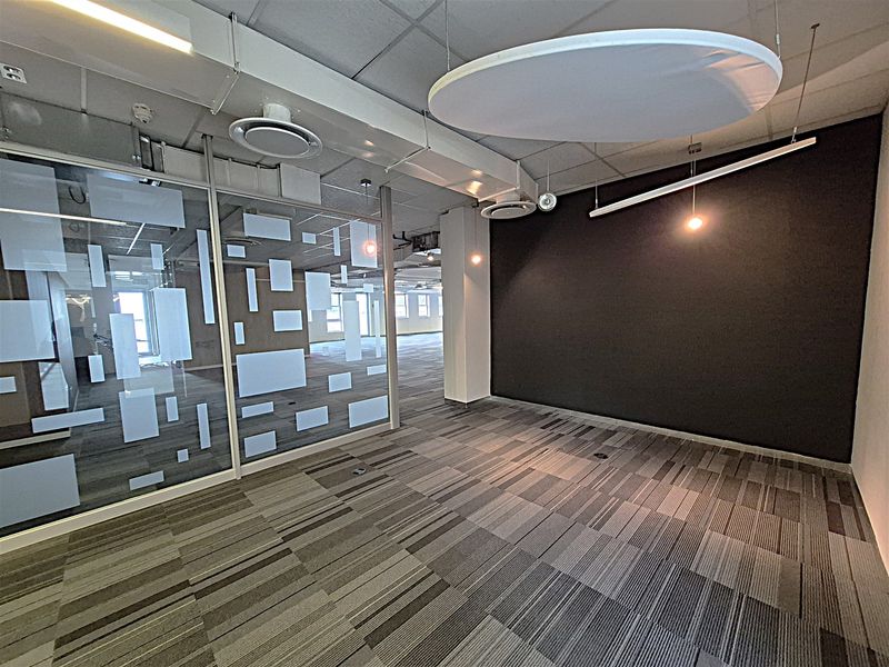 Modern open-plan office space featuring glass partitions, suspended acoustic ceiling panels, carpeted flooring, and integrated climate control systems.