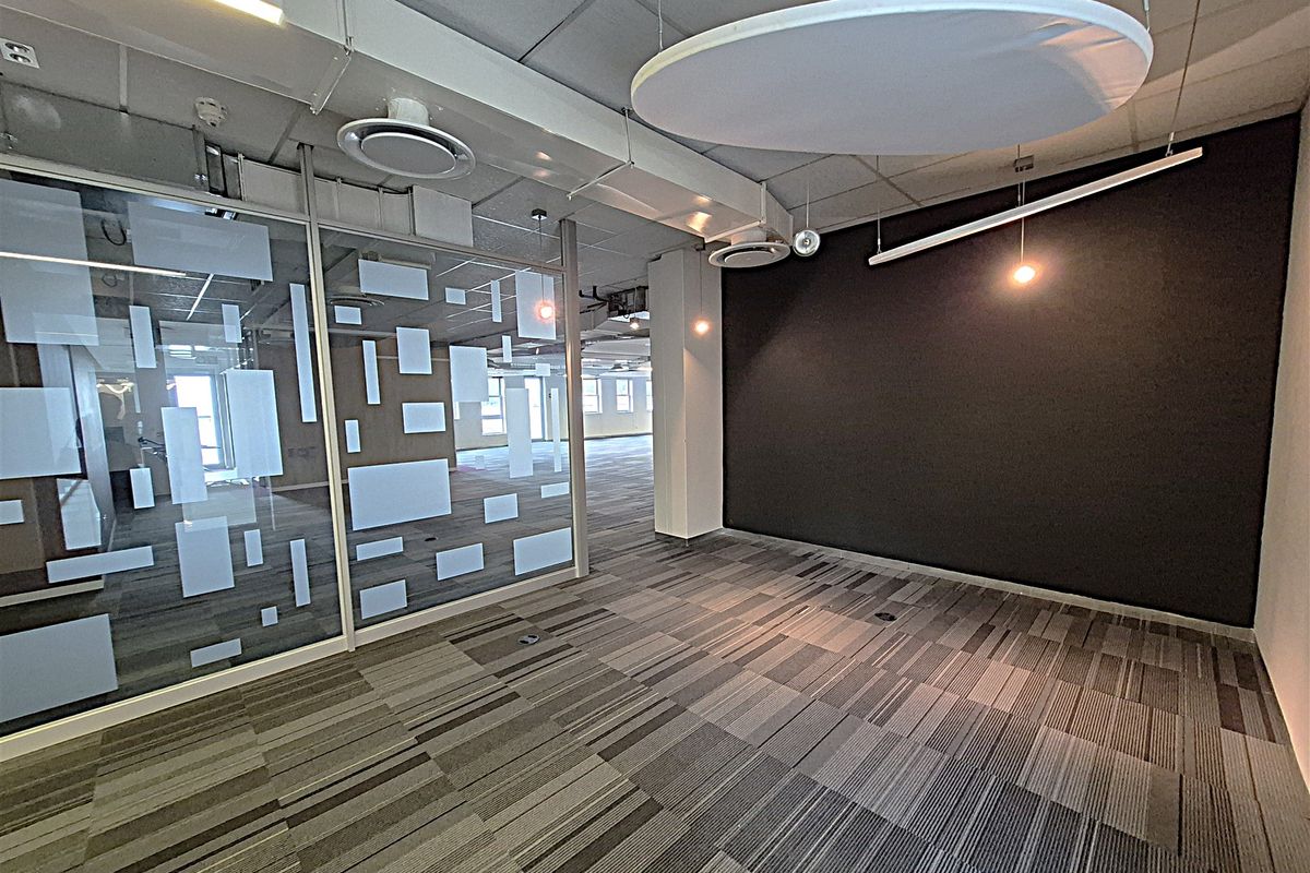 Modern open-plan office space featuring glass partitions, suspended acoustic ceiling panels, carpeted flooring, and integrated climate control systems.