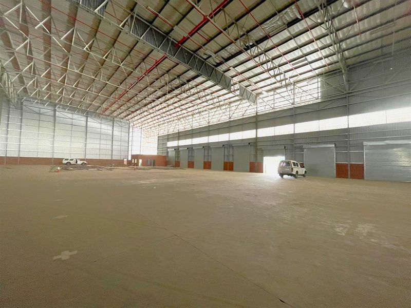 Spacious industrial warehouse featuring high-clearance steel truss roofing, fire sprinkler system, concrete flooring, and multiple roller shutter doors for efficient access.