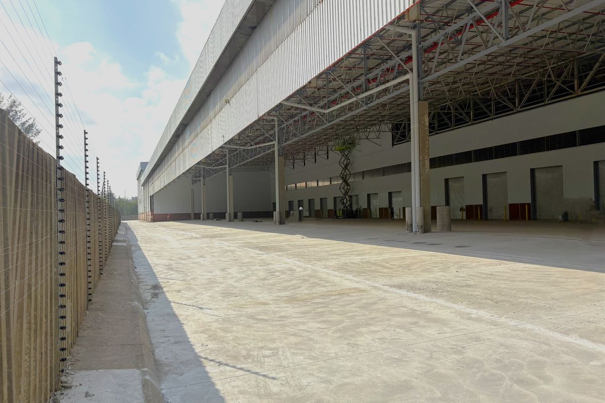 Large industrial warehouse exterior featuring a spacious concrete yard, steel portal frame construction, metal cladding, and multiple roller shutter loading bays.