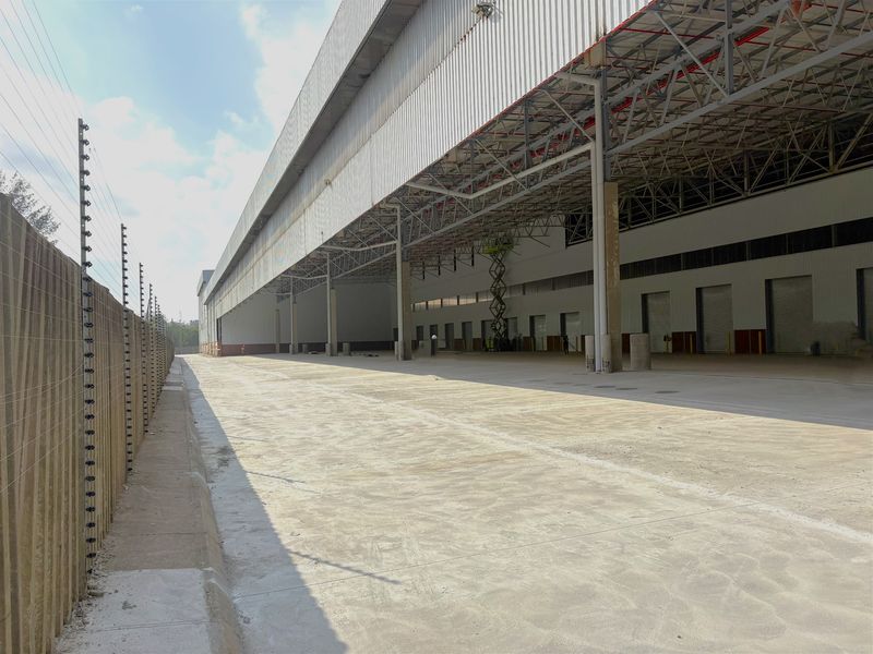 Large industrial warehouse exterior featuring a spacious concrete yard, steel portal frame construction, metal cladding, and multiple roller shutter loading bays.