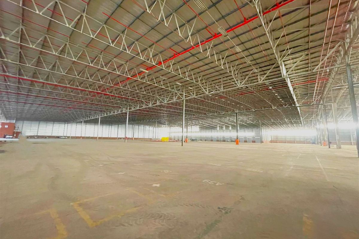 Expansive industrial warehouse space featuring high ceilings with exposed steel trusses, fire sprinkler system, and durable concrete flooring throughout.