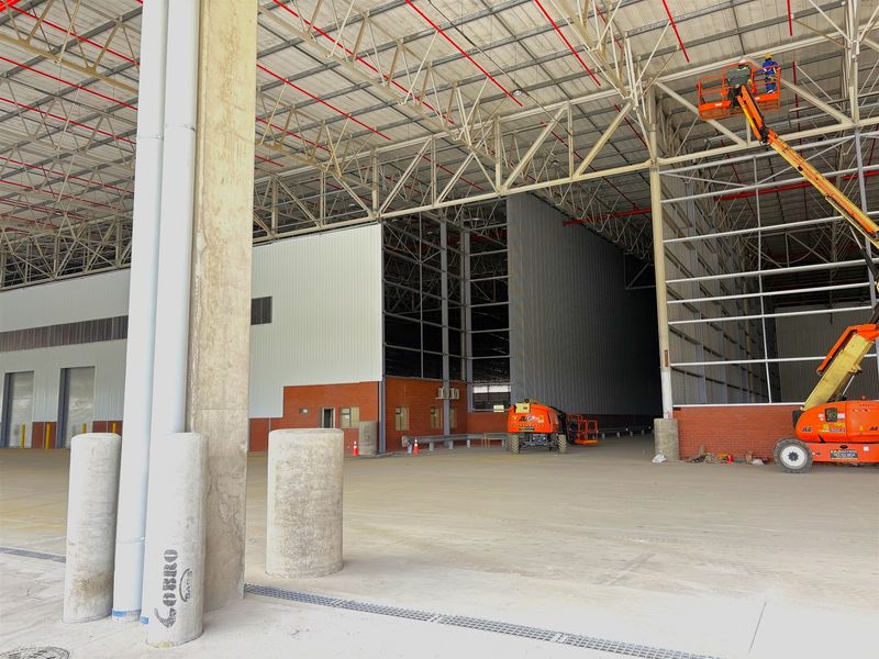 Spacious industrial warehouse interior featuring high-clearance steel truss roofing, concrete flooring, and integrated fire sprinkler systems, currently under final construction or maintenance.