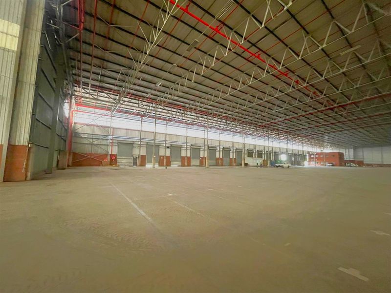 Expansive industrial warehouse space featuring high ceilings, steel portal frame construction, concrete flooring, and multiple roller shutter doors for efficient logistics and storage operations.