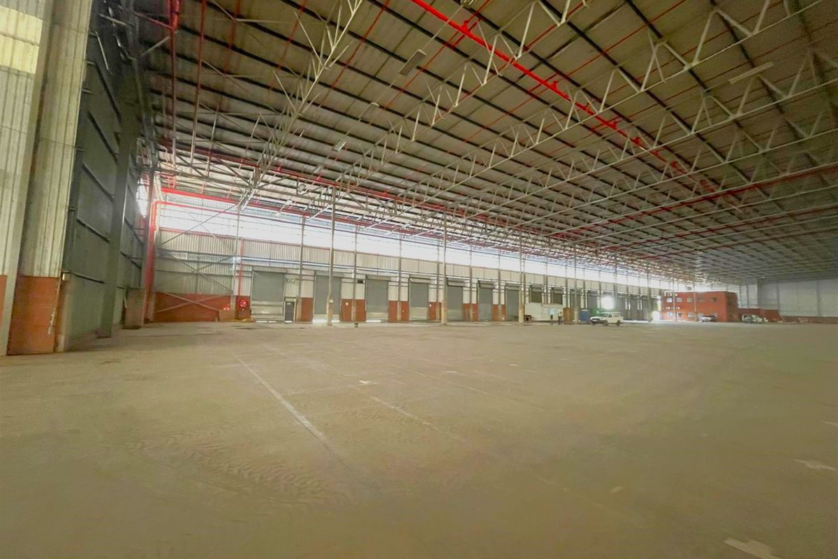 Expansive industrial warehouse space featuring high ceilings, steel portal frame construction, concrete flooring, and multiple roller shutter doors for efficient logistics and storage operations.